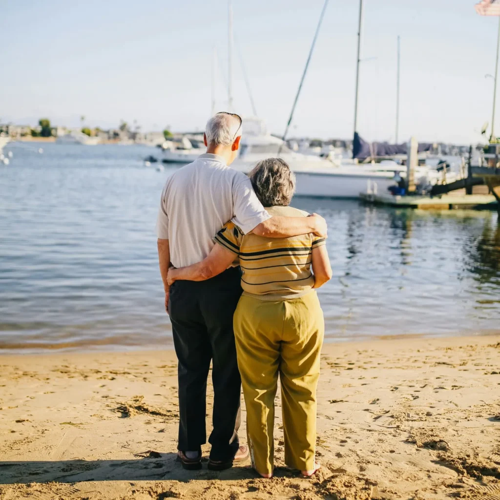 Älteres Ehepaar steht am Strand dank mobilem Hausnotrufgerät